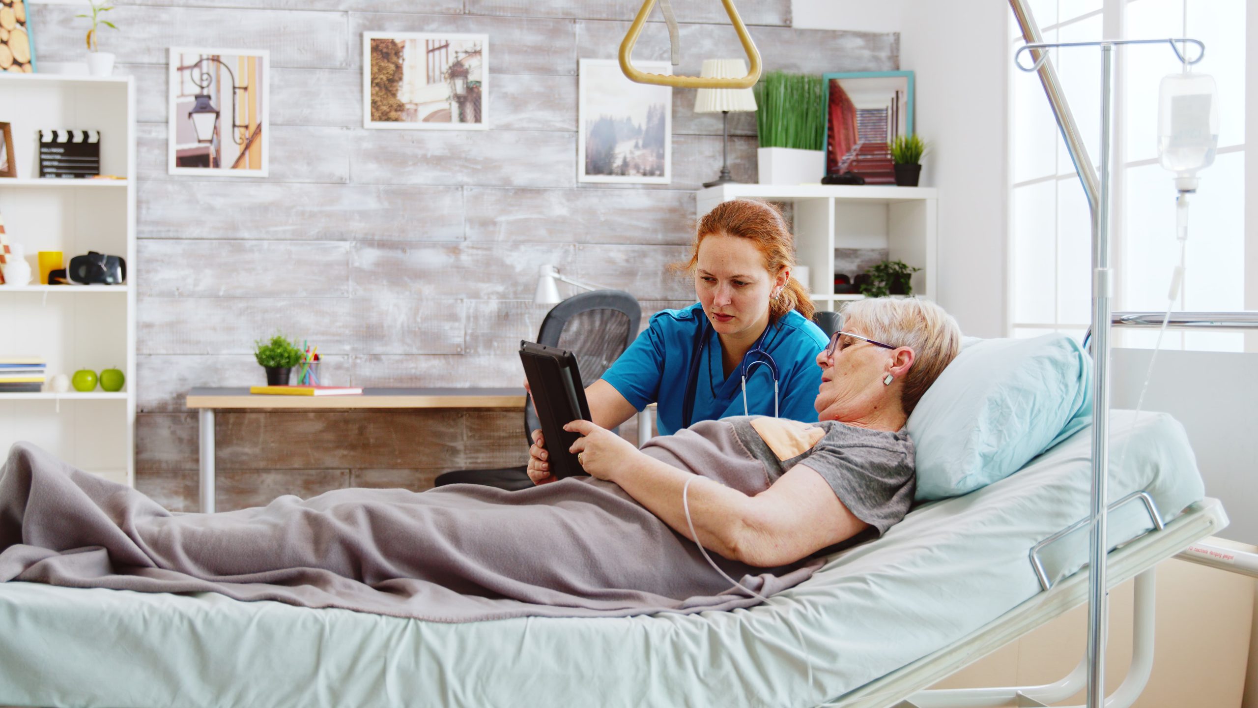 female-caregiver-helps-old-disabled-woman-lying-hospital-bed-use-digital-tablet-pc-bright-room-with-big-windows